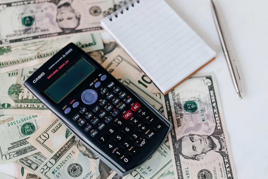 Boligrafo, cuaderno y calculadora sobre dinero en mesa blanca evidenciando los beneficios fiscales de las inversiones en el sector inmobiliario