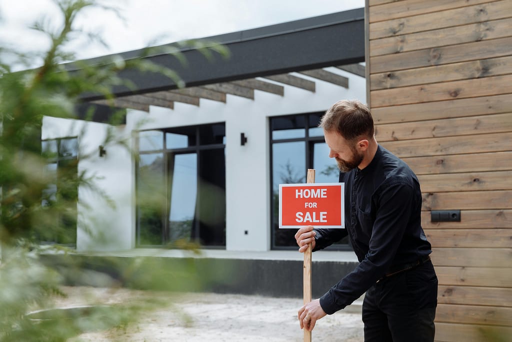 Hombre vestido de negro colocando un cartel de venta de una casa.